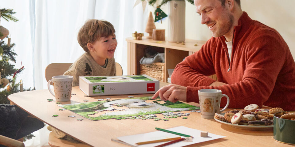 Far og søn sidder ved et bord og lægger et puslespil, omgivet af julepynt og julebag